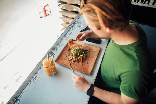 High angle view of a young Caucasian male sat in an Indonesian restaurant eating chicken satay with a fruit smoothie.