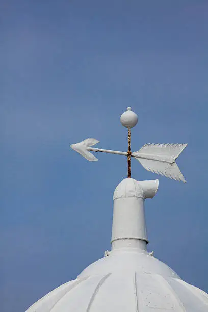 Rooftop of a lighthouse with direction arrow against the blue sky.