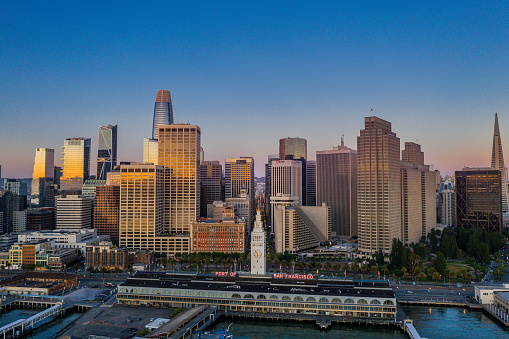 An aerial view of the San Francisco skyline look over the Ferry Terminal up Market Street. Sunrise light shines off the glass skyscrapers.