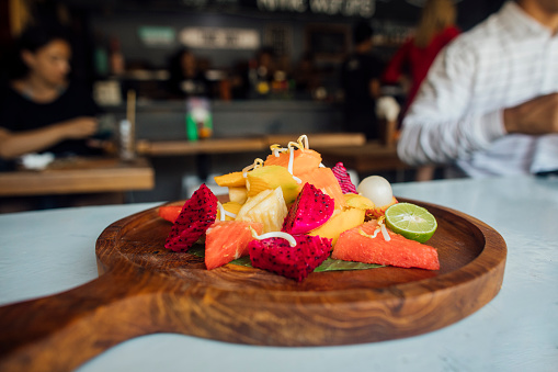 A side view of a well presented, vibrant fruit salad on a wooden dish in a restaurant.
