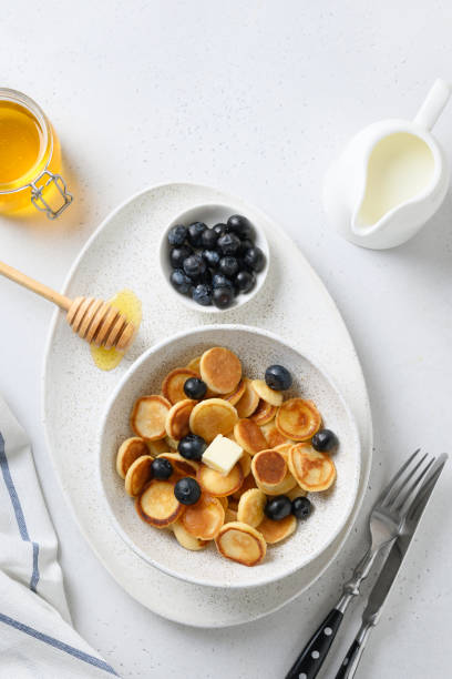 istock Tiny cereal pancakes with blueberry and honey on white background. View from above. 1227586330