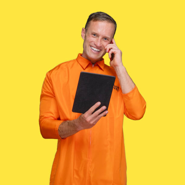 istock Criminal standing in front of yellow background wearing jumpsuit and using touch screen 1227588429