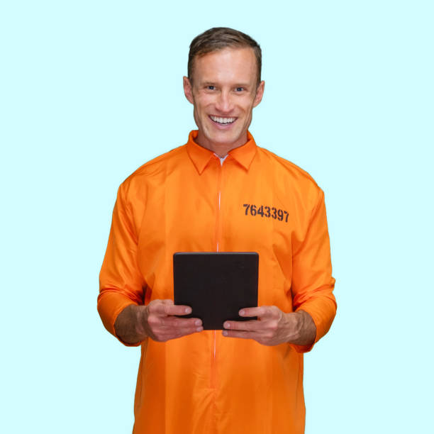 Criminal standing in front of blue background wearing jumpsuit and using touch screen