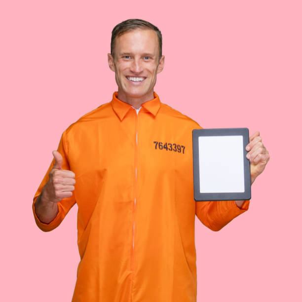istock Criminal standing in front of colored background wearing jumpsuit and using digital tablet 1227588517