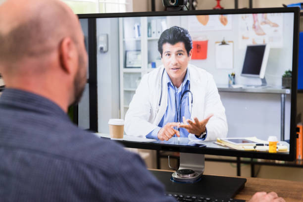 Unrecognizable man teleconferences with doctor An unrecognizable mid adult man teleconferences with his doctor from his home office. over the shoulder view photos stock pictures, royalty-free photos & images