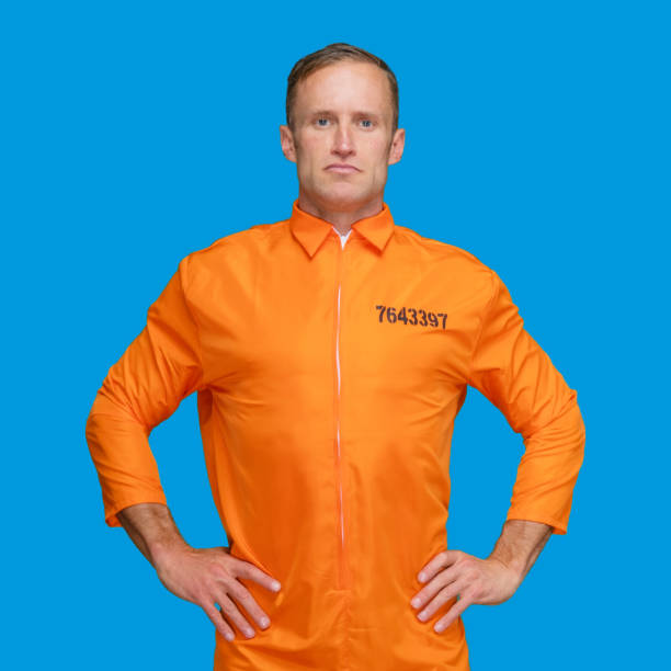 istock Criminal standing in front of blue background wearing jumpsuit 1227589216