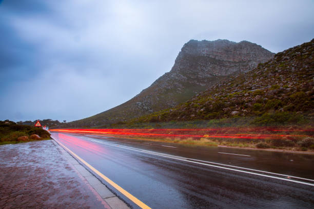 A Wet mountainside road with blurred light trails. A Wet mountainside road with blurred light trails from passing cars, in the Overberg region in Cape Town, South Africa. gordons bay stock pictures, royalty-free photos & images