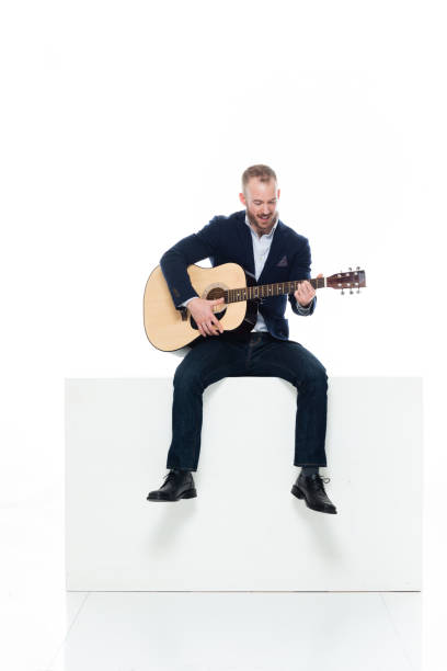 guitarrista masculino caucásico descansando frente a fondo blanco usando pantalones y sosteniendo guitarra acústica - suit jeans men musician fotografías e imágenes de stock