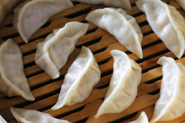 Close-up image of Momos (South Asian dumplings), white flour and water dough filled with chicken and mixed vegetables in bamboo steamer being cooked, elevated view Stock photo showing a restaurant meal of steaming dumplings (Momos) filled with mixed vegetables and chicken in bamboo steamer. chinese dumpling stock pictures, royalty-free photos & images