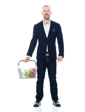 One person of with with beard caucasian male businessman standing in front of white background wearing jeans who is laughing who is shopping and holding groceries