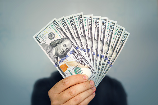 Hands holding dollar cash. 1000 dollars in 100 bills in a man's hand close-up on a dark background.