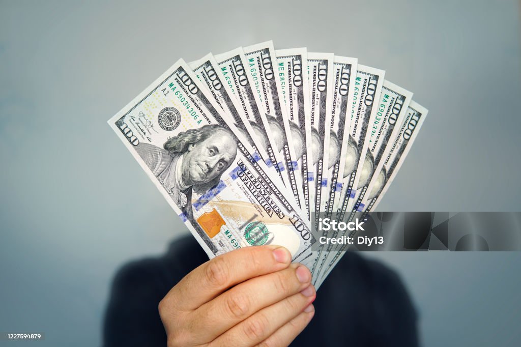 1000 dollars in 100 bills in a man's hand close-up on a dark background. Hands holding dollar cash Hands holding dollar cash. 1000 dollars in 100 bills in a man's hand close-up on a dark background. Currency Stock Photo