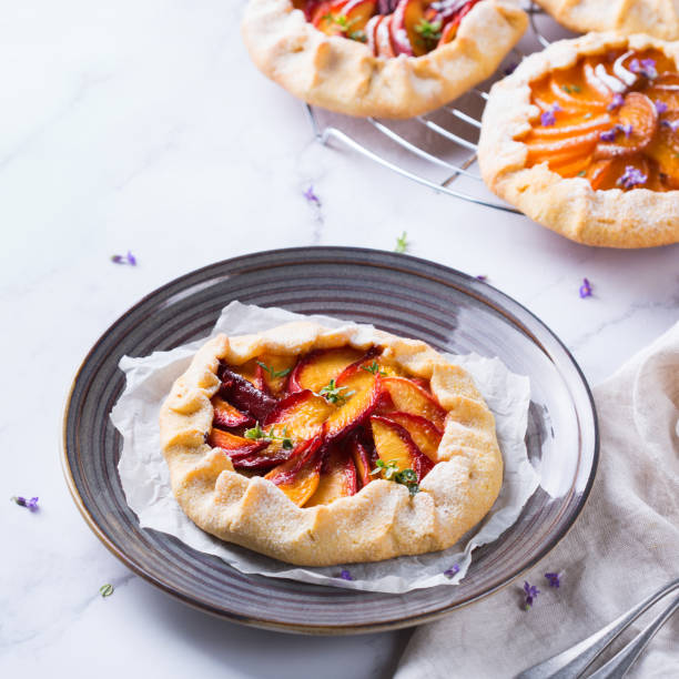 Homemade seasonal summer fruit galette, tart, pie with nectarines, peaches Homemade small nectarine, peach, apricot galette, tart, seasonal summer open pie with aromatic herbs. Healthy and tasty bakery product, dessert with ripe fruits. Top view, flat lay background galette stock pictures, royalty-free photos & images