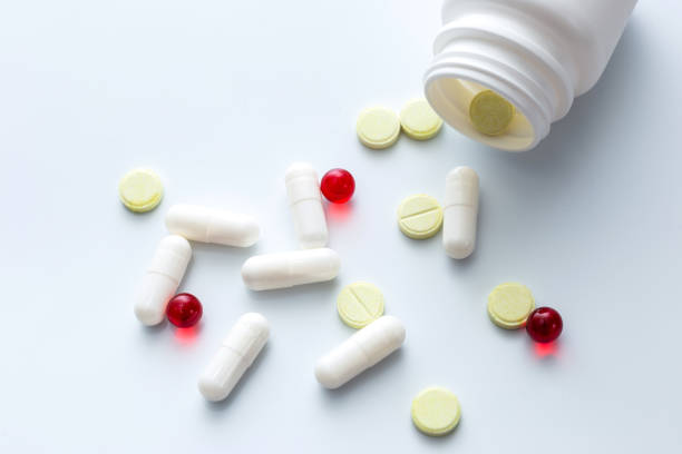 istock Assorted tablets and capsules spilled out of a white bottle. White background. 1227599771