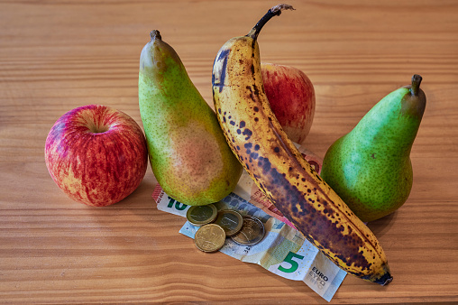 Fruit lying together with European banknotes and coins on a wooden background.