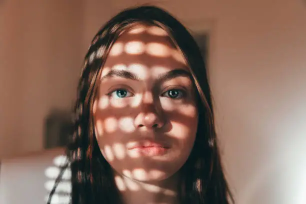 Light and Shade. Attractive young teenage woman with bright blue eyes looking towards the camera. Light and shade of grid illuminating the face. Teenage Female Portrait.