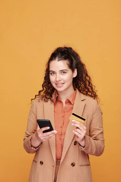 istock Contemporary young female with smartphone and plastic card going to make order 1227609974
