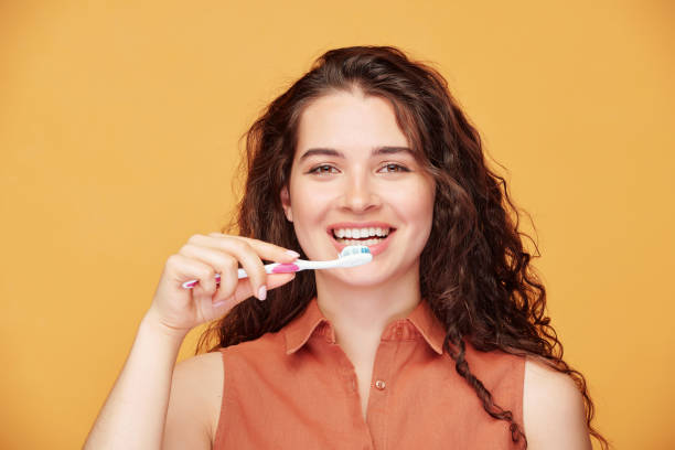 jeune femme de brune riante avec le sourire sain se brossant ses dents - human mouth human teeth indoors young women photos et images de collection