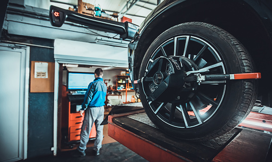 One man, mechanic in auto repair shop, wheel alignment equipment on a car wheel in a repair station.