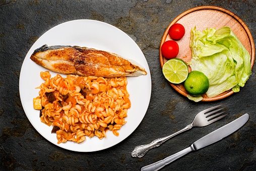 High angle view of fried fish wheel on a plate served ready to eat. Also healthy salad with lemon,cherry tomato and lettuche.