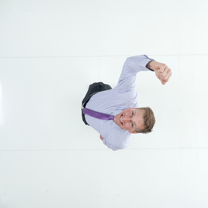 Aerial view of aged 20-29 years old with short hair caucasian male businessman standing in front of white background wearing shirt who is laughing and celebrating and showing fist who is and doing fist pump