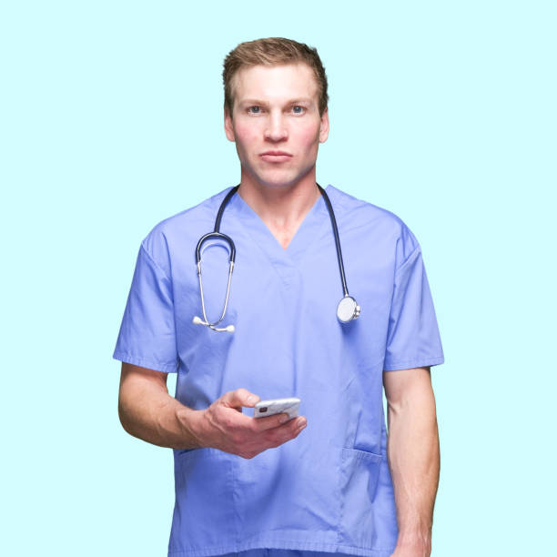 kaukasiska ung man som står framför blå bakgrund och använder smart telefon - nurse on phone serious bildbanksfoton och bilder