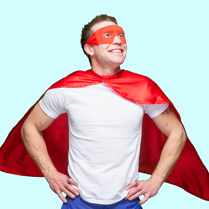 Front view of with brown hair caucasian young male hero standing in front of white background wearing costume who is conquering adversity with hand on hip