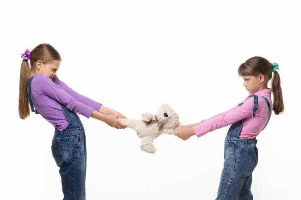 istock Girls pull teddy bear at each other on white background 1227613663