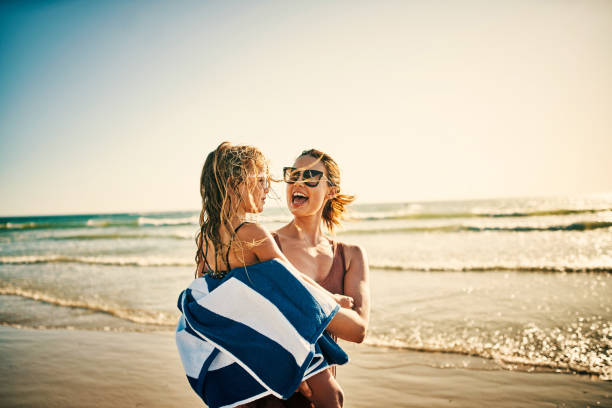 Summertime means lots of fun family memories Shot of a young woman wrapping her adorable little girl in a towel at the beach woman wrapped in bath towel stock pictures, royalty-free photos & images
