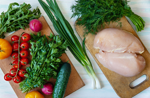 Balanced nutrition on a light background, fresh vegetables and herbs on a cutting board and raw chicken fillet, top view with place for text