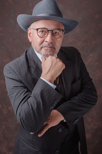 Mature gentleman posing for the camera in a dark brown suit with stripes and hat