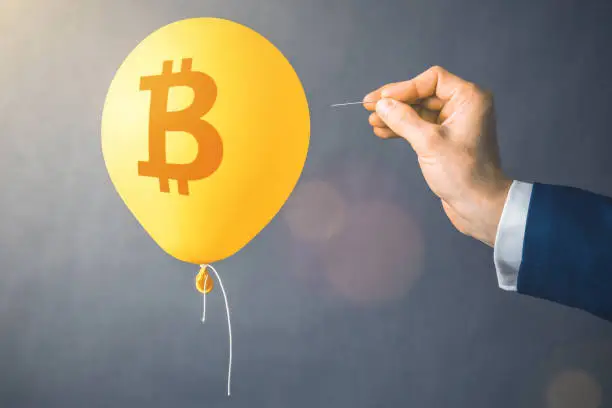 Bitcoin cryptocurrency symbol on yellow balloon. Man hold needle directed to air balloon. Concept of finance risk.