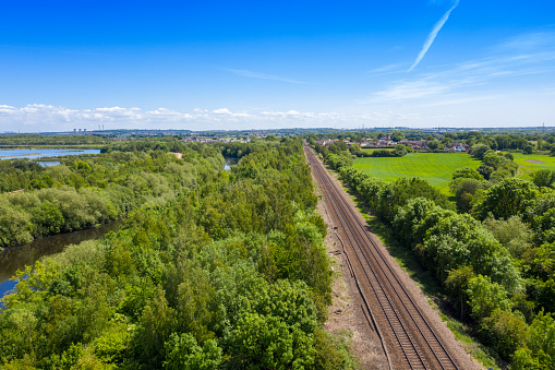 Beautiful aerial photo of train tracks going in to the distance, taken with a drone on a sunny summers day with green trees and wooded area along side the train tracks in the town of Methley in Leeds