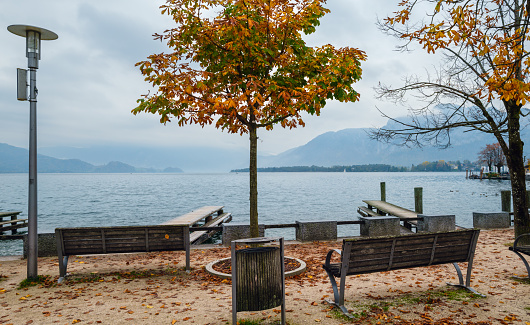 Beach and lake of Lac Beauport during autumn day where we see small pier in foreground and colorful tree mountain in background