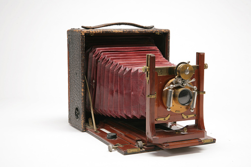 4x5 large format view camera with gears and levers on lens. Red leather bellows extends out behind the lens