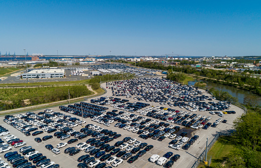Panoramic aerial view of a parking lot fulfilled by new cars prepared for shipment to resellers and car dealers.