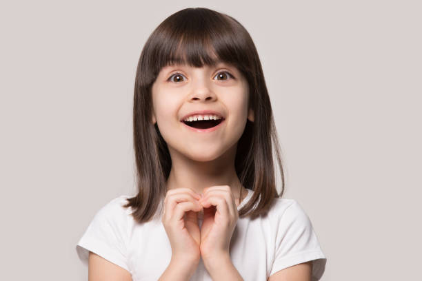 Cheerful excited little girl showing heart love gesture. Close up head shot portrait cheerful excited small 6 years old girl looking at camera, showing heart gesture, isolated in grey studio background. Overjoyed cutie feeling happy achieving wished goal. russian ethnicity stock pictures, royalty-free photos & images