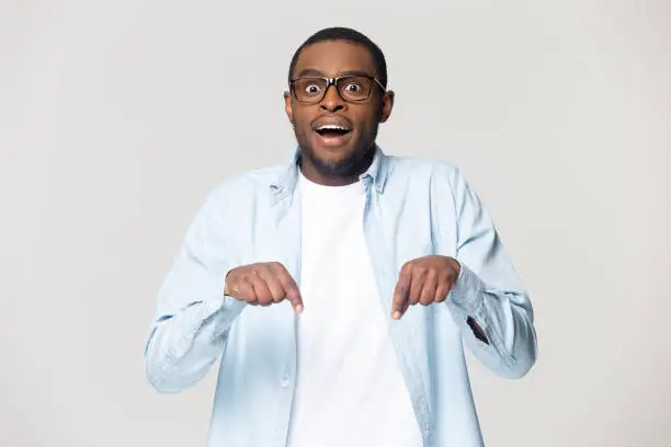 African open mouth make big eyes gawp look at camera pointing fingers down isolated on grey background, advertising new products showing drop in prices and rebate, seasonal sales concept