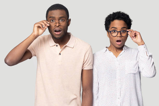 Confused african couple gawp at camera open mouth lowering glasses African ethnicity young confused couple pose isolated on grey white studio background, girl and guy gawp at camera open mouth lowering glasses feeling amazement, stunned or surprising by news concept gawp stock pictures, royalty-free photos & images
