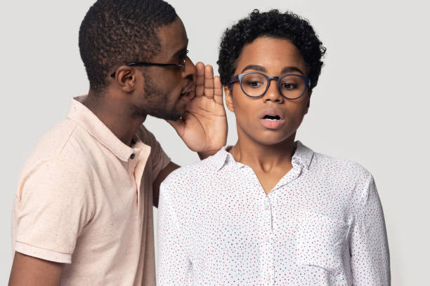 African guy whispering to ear of girl secret, studio shot African guy chatterbox shares secret whispering to ear of amazed stunned mixed-race girl shocking news, young attractive couple gossiping spread rumors concept, studio shot isolated on gray background whisper men stock pictures, royalty-free photos & images