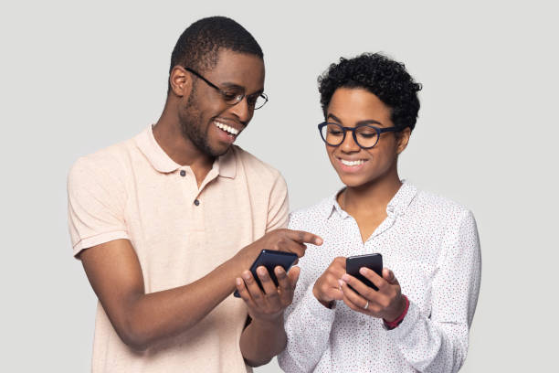 アフリカのカップルは、インターネットスタジオショットで楽しんでスマートフォンを保持します - video sharing ストックフォトと画像