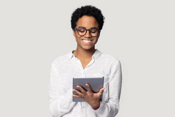 African young woman holding digital tablet isolated on gray background, student busy with assignment using educational websites useful applications, freelancer do remote distant work on-line concept