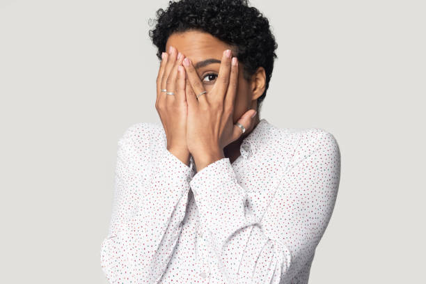 Afraid african woman hiding face with hands peeping through fingers Afraid african woman isolated on gray background looking shy or terrified covering hiding her face with hands peeping through fingers is shocked by horror movie or frightened by what she saw concept camera covers pictures stock pictures, royalty-free photos & images