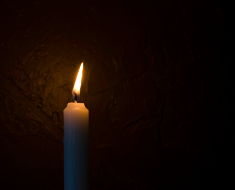 A candle burns in a dark room by the wall