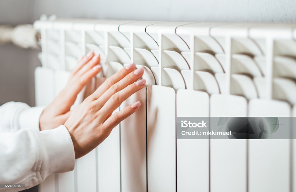Woman warms up hands over heater. Woman warms up hands over heater. Concept of the need for good central heating. Radiator - Heater Stock Photo