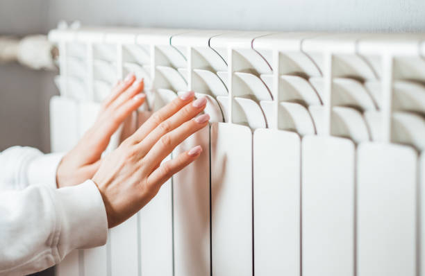 Woman warms up hands over heater. stock photo