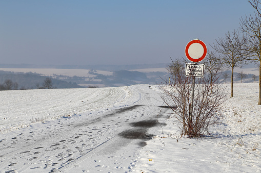 Winter field road on a clear sunny day. The inscription under the sign in German: Agricultural vehicles only