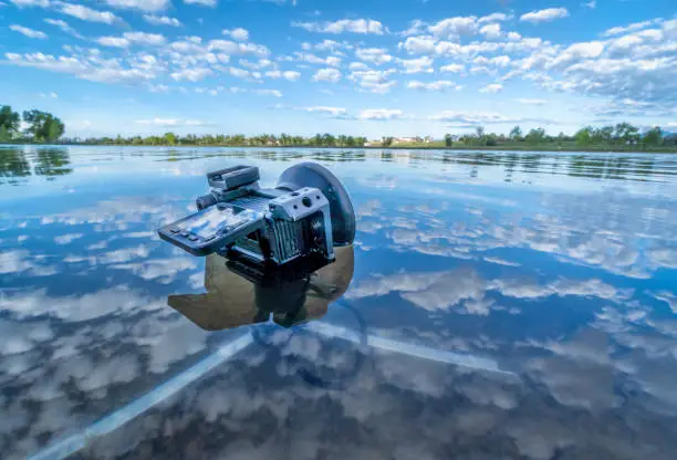 small waterproof action camera in a rugged cage partially submerged with a mini tripod in a calm lake, morning spring scenery in Colorado
