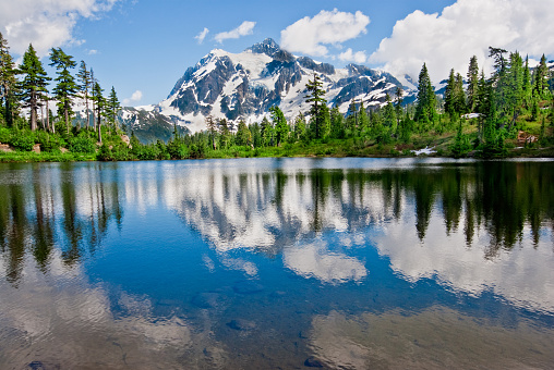The North Cascades is a vast wilderness of conifer-clad mountains, glaciers and lakes. It is one of the more remote wilderness areas in the Continental United States. Because of its striking beauty, Mount Shuksan in the North Cascades, is one of the most photographed mountains in the world. This picture of Mount Shuksan reflected in the water was taken from Picture Lake in the Mount Baker National Forest in Washington State, USA.