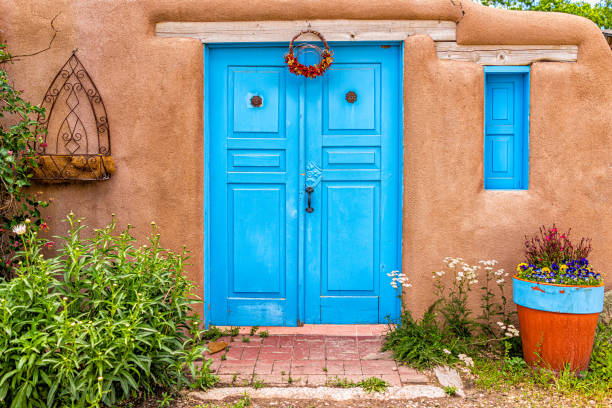 New Mexico traditional colorful architecture with blue turquoise adobe color painted door and ristras decorations at entrance garden New Mexico traditional colorful architecture with blue turquoise adobe color painted door and ristras decorations at entrance garden blue house red door stock pictures, royalty-free photos & images